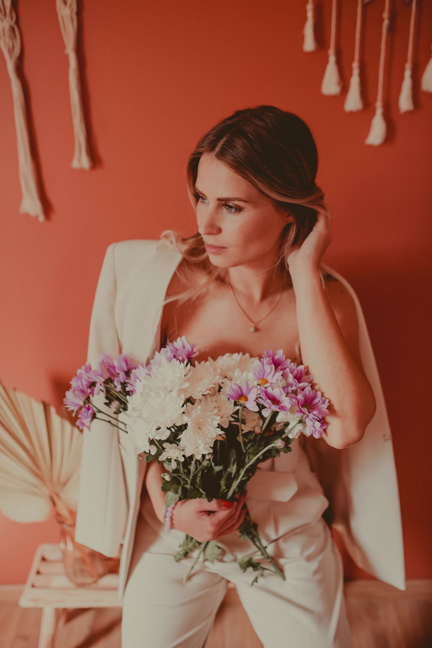 Romantic portrait series with pink flowers and macrame details against a coral-colored wall.