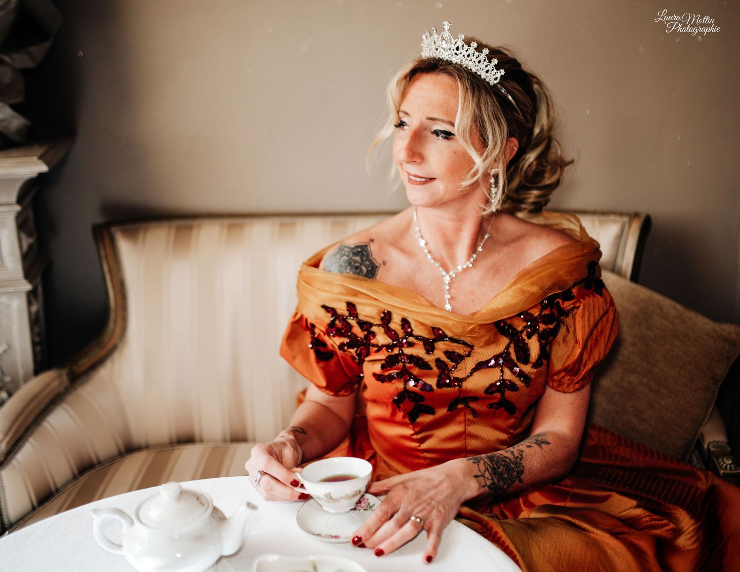 Person in elegant period dress holding a teacup during a vintage-themed event.
