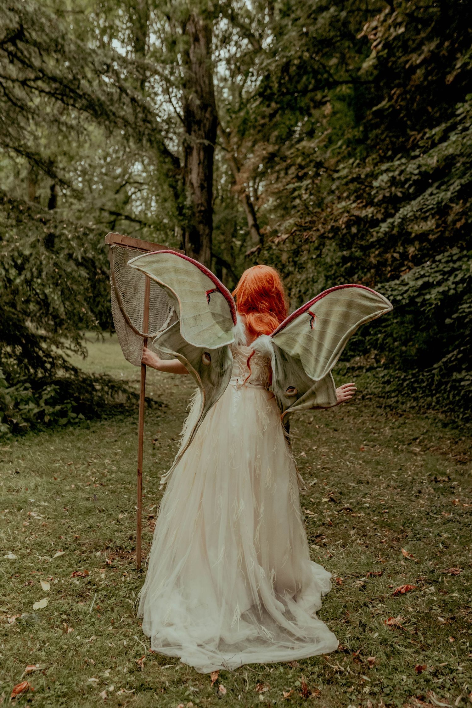 Ethereal outdoor fairy photoshoot with translucent wings in forest setting.