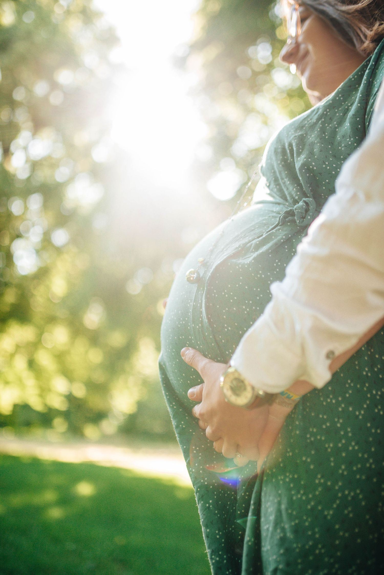 Side profile of pregnant belly in natural sunlit setting with bokeh effect.