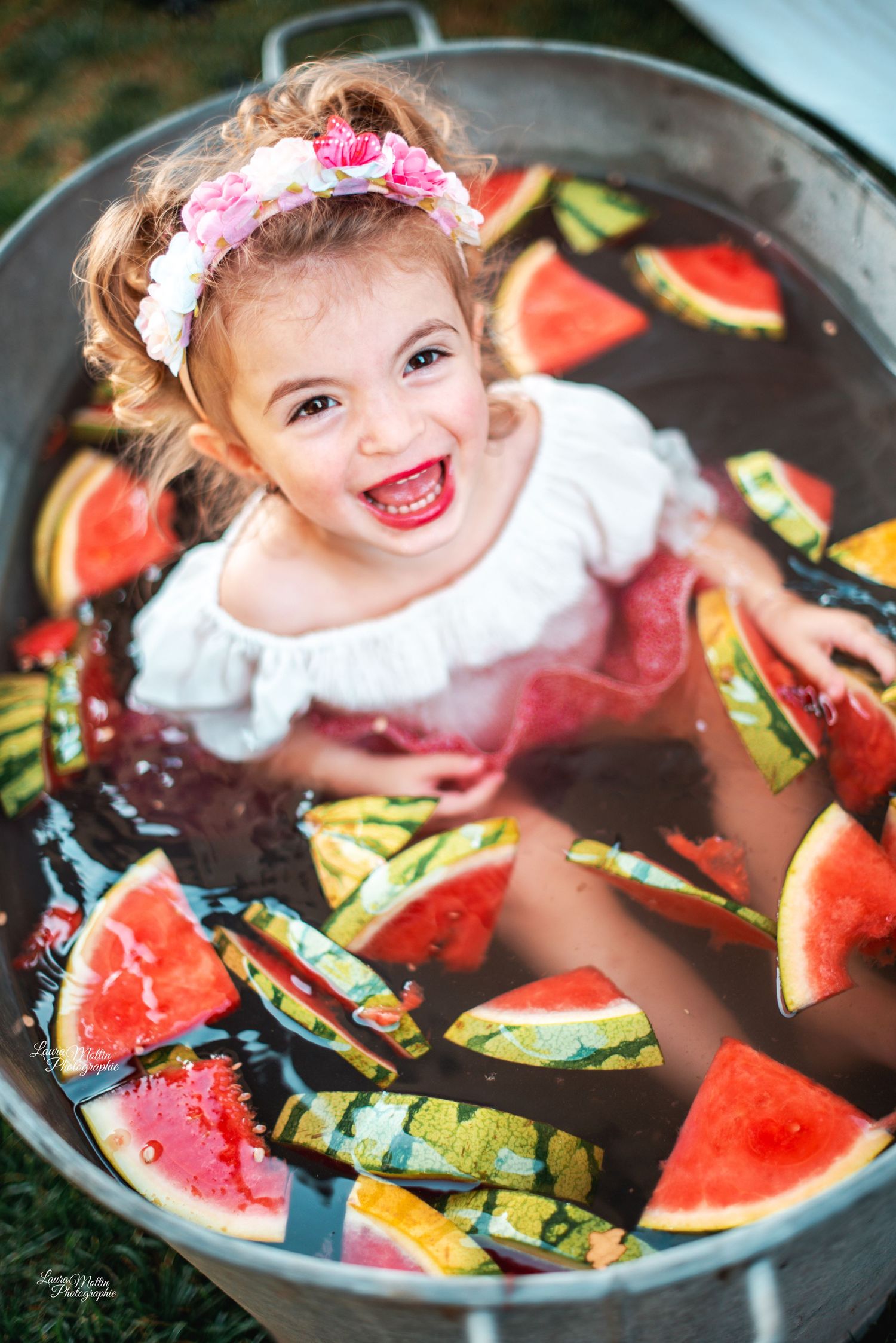 Creative portrait in a watermelon-filled bath with bright pink flowers and floating fruit slices.