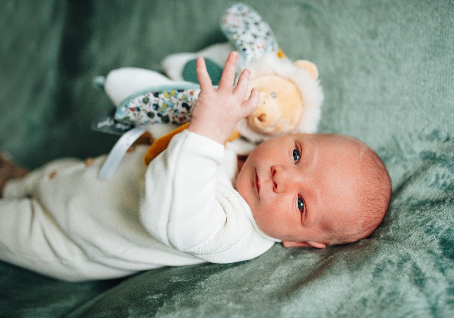 Newborn baby wearing white outfit lying on green textured surface in professional photo series.