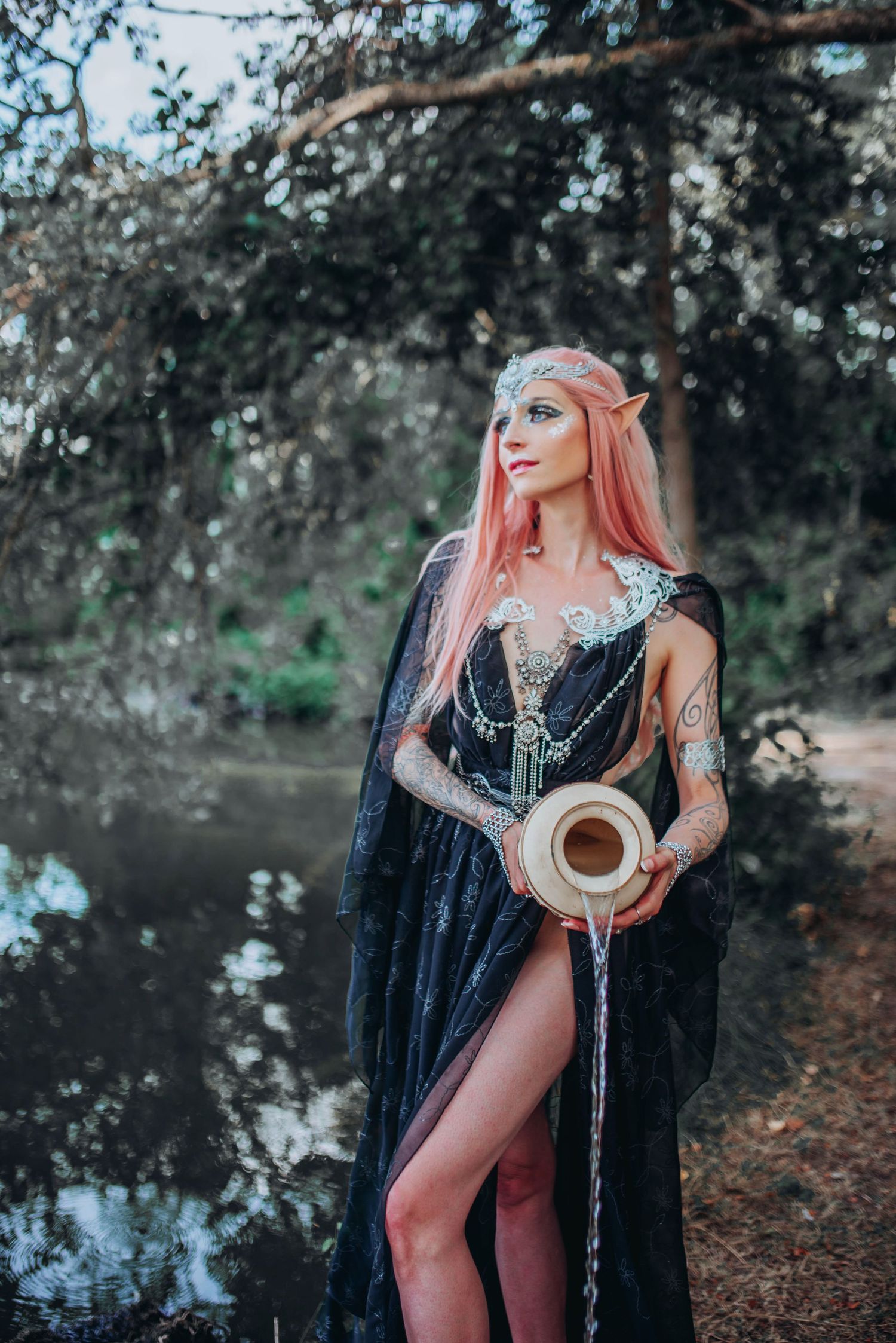 Ethereal woodland photoshoot with flowing black cape and pink hair against a misty lake backdrop.