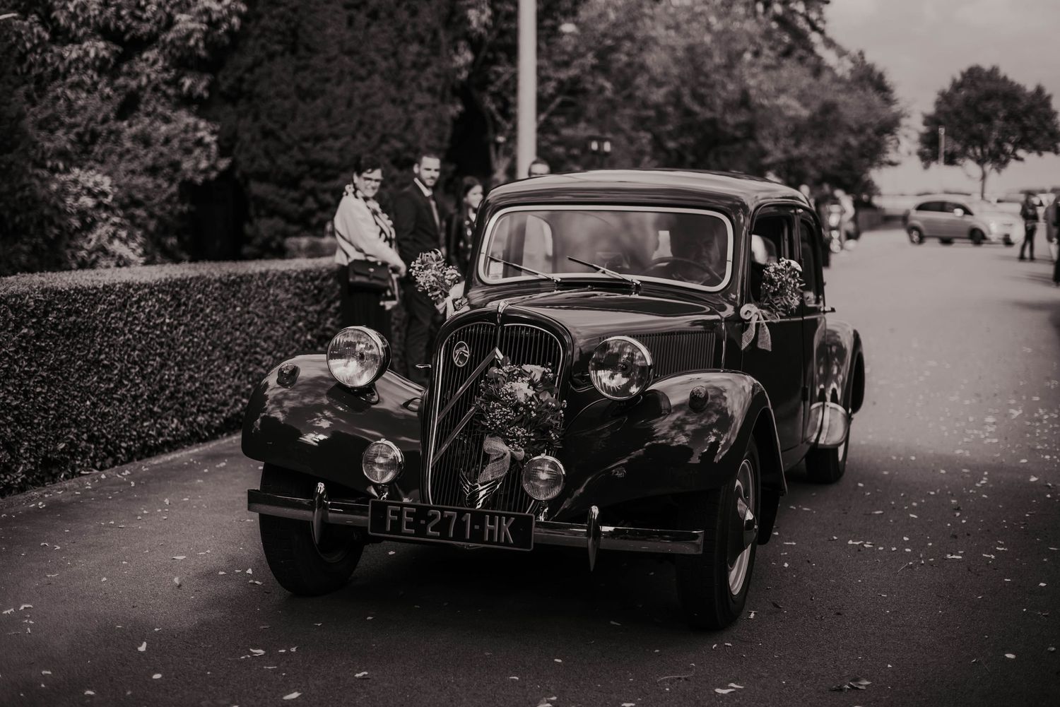 A vintage black car decorated for a wedding parked on a tree-lined street.