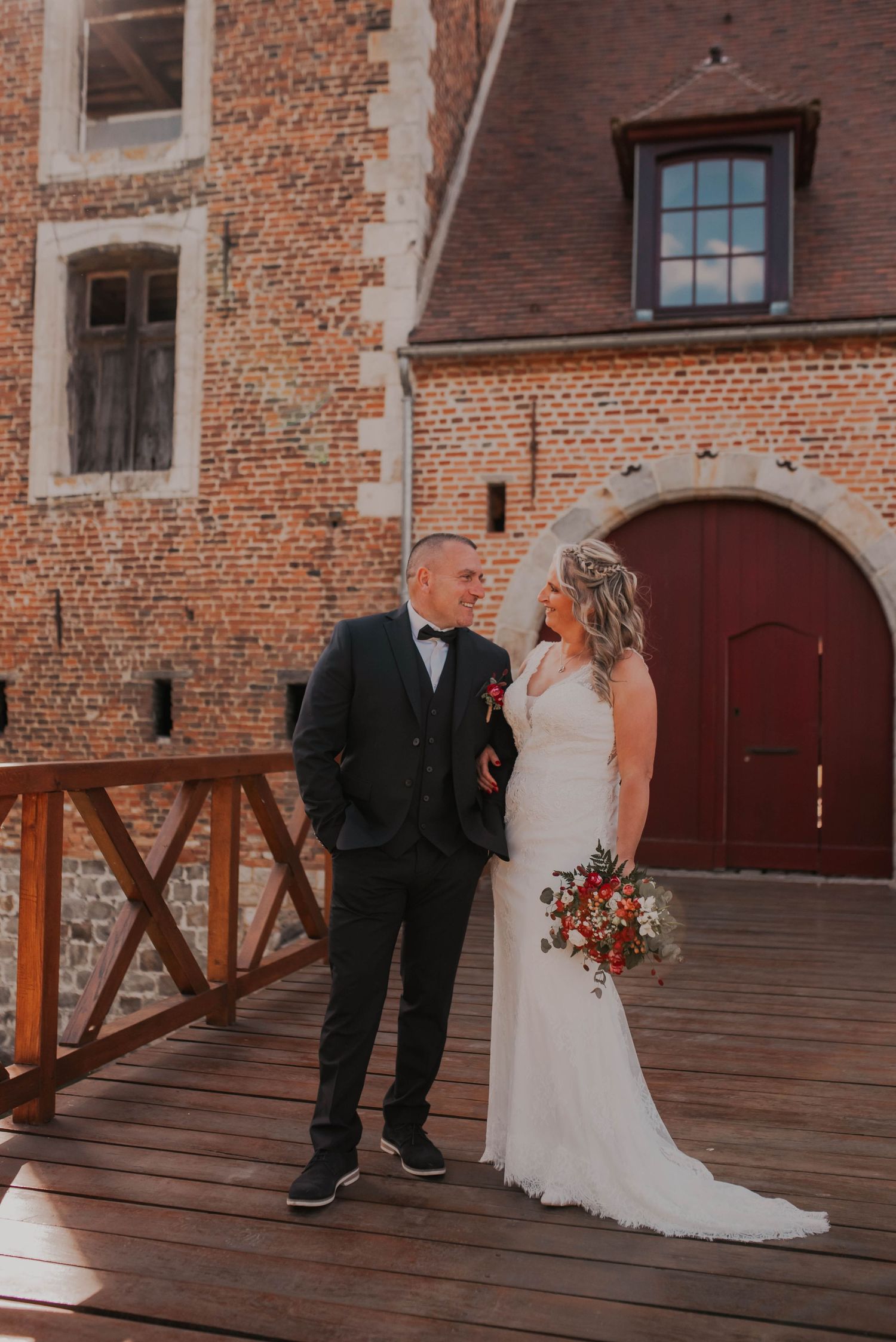 A couple poses on a wooden deck against a rustic brick building backdrop.
