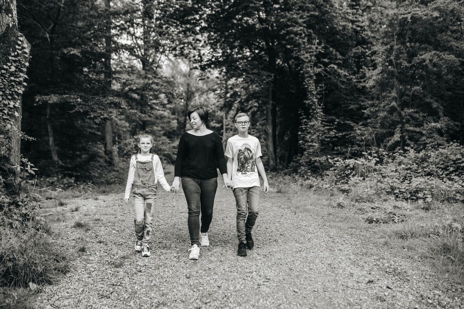 Family walking together through wooded path in black and white.