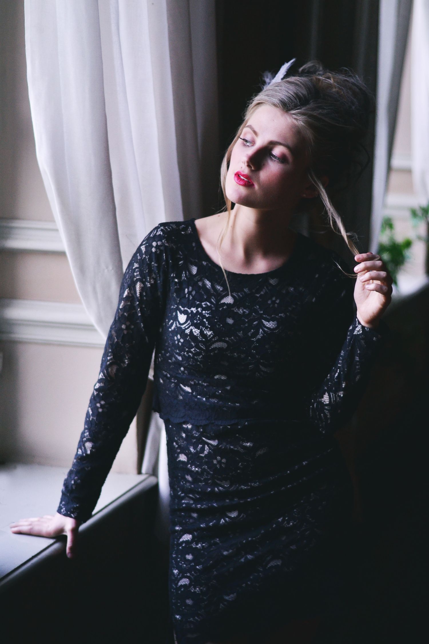 Dramatic window light portrait in black lace dress with vintage styling.