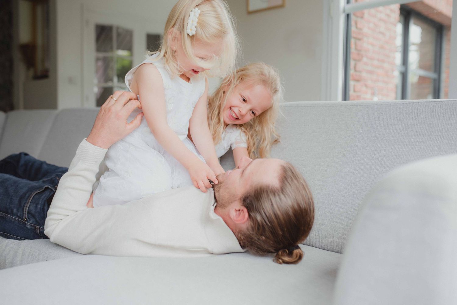 Playful moments captured on white couch in bright living room setting.