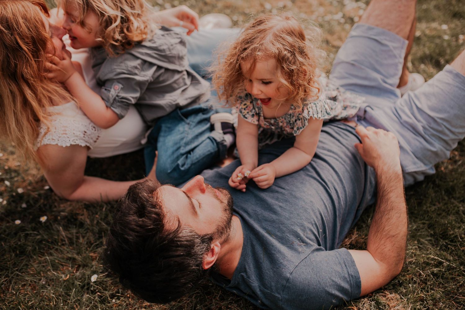 A family lying together in a grassy meadow during a casual outdoor photoshoot.