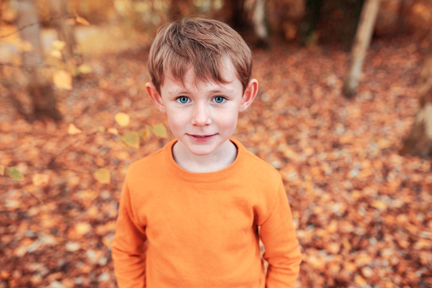Outdoor autumn portraits with matching orange clothing among fallen leaves.