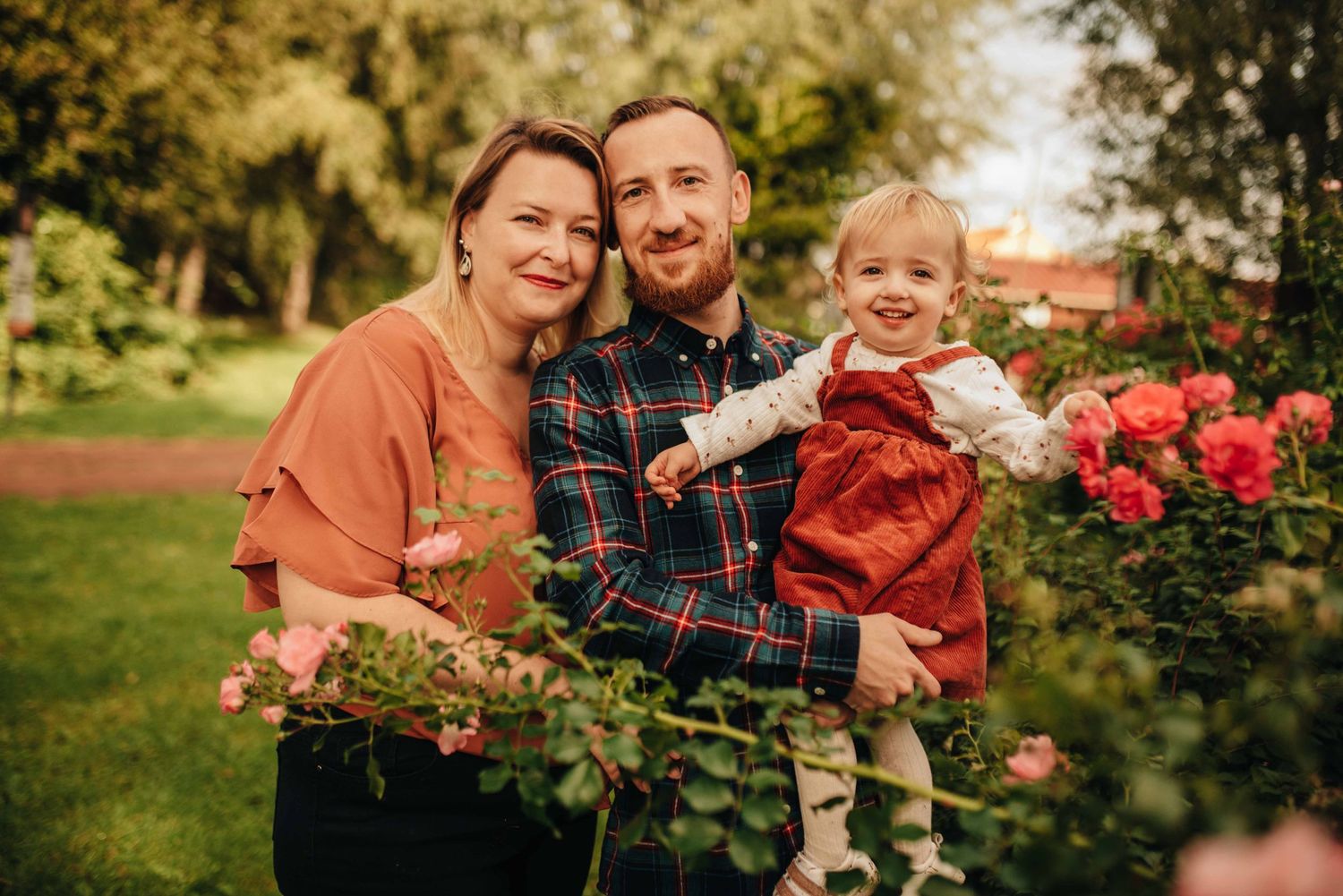 Family portrait session among blooming rose bushes in a garden setting.