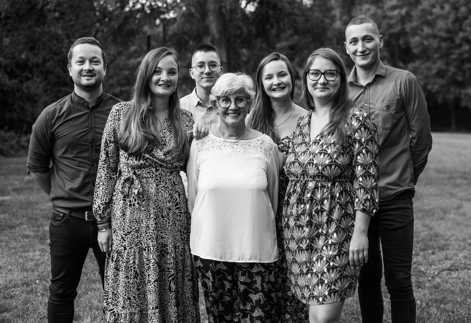 Group portrait of people standing together outdoors with trees in background.