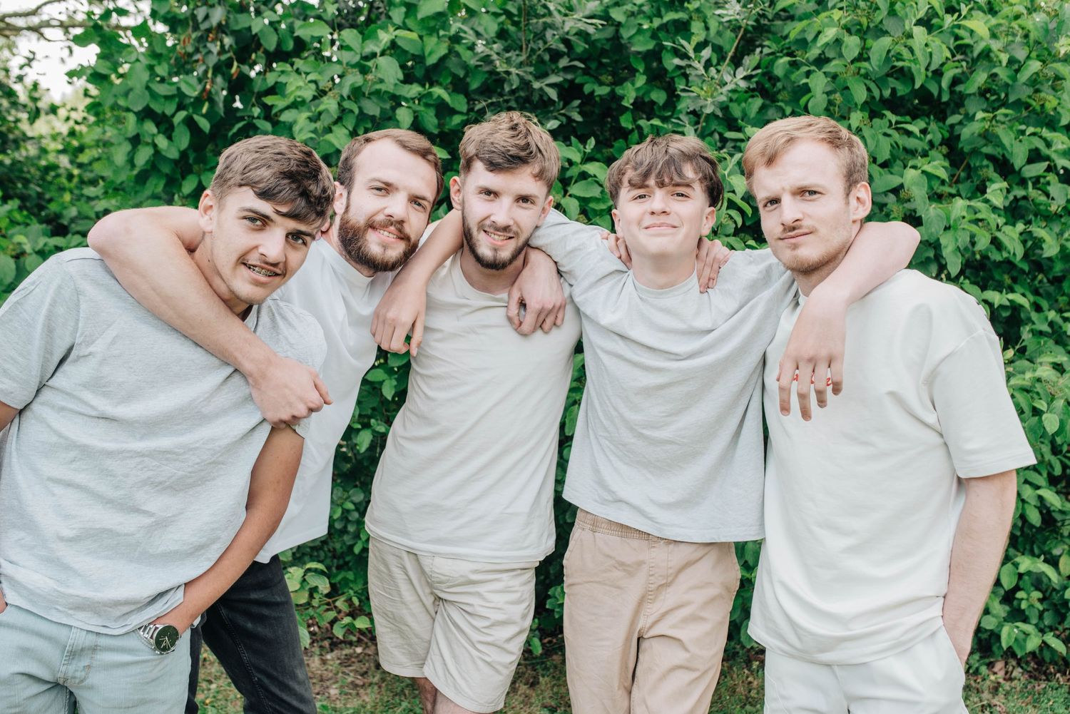 Group photo of people wearing light colored clothing posing together outdoors in a green garden setting.