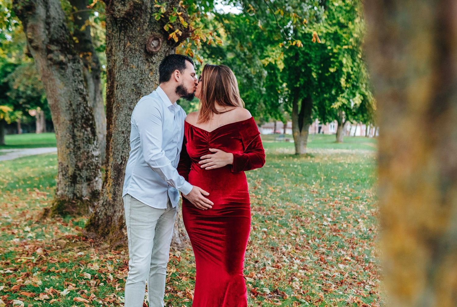 Romantic autumn maternity photo session in a park with red dress and fallen leaves.