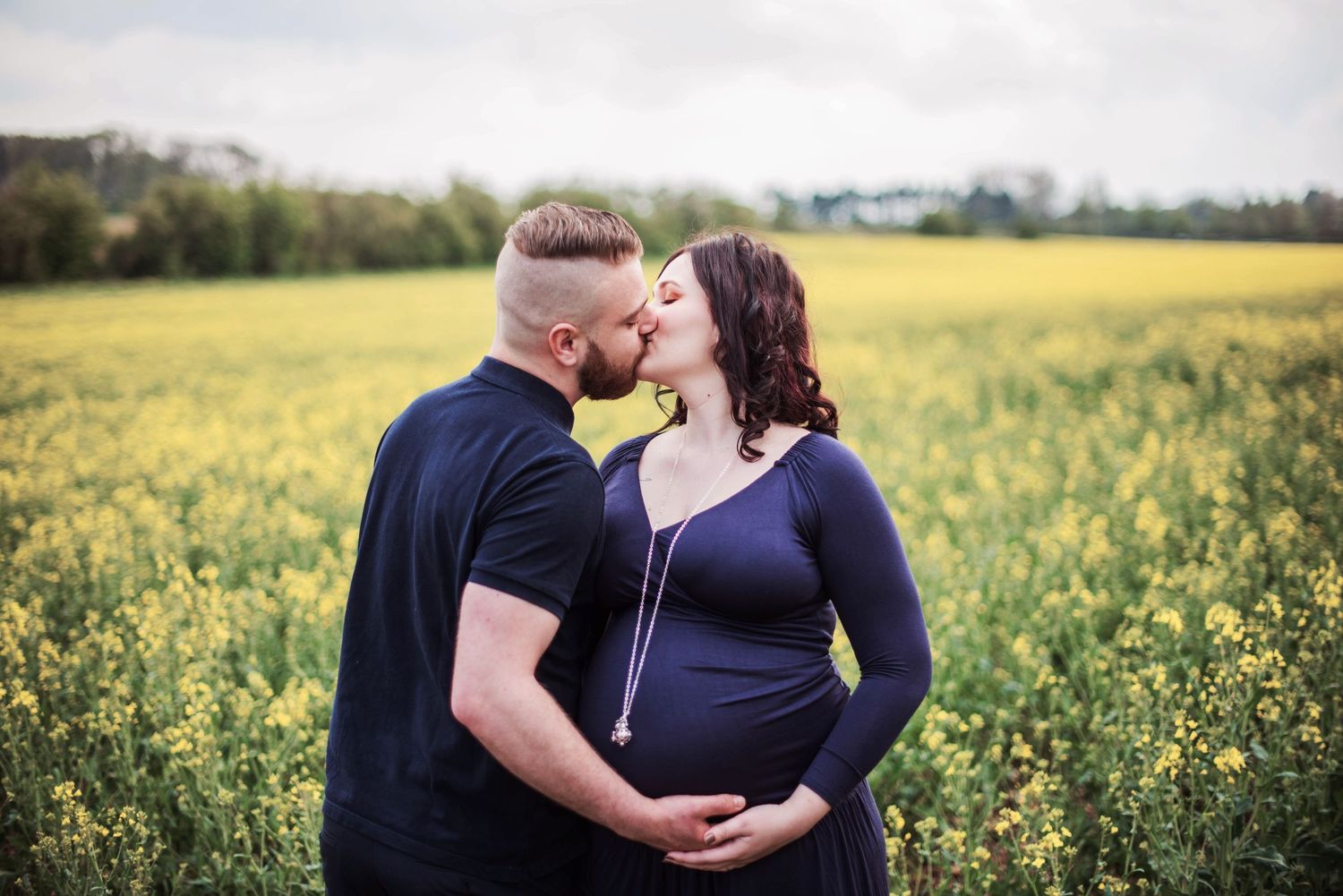 Couple sharing an intimate moment in a blooming yellow canola field during maternity photoshoot.