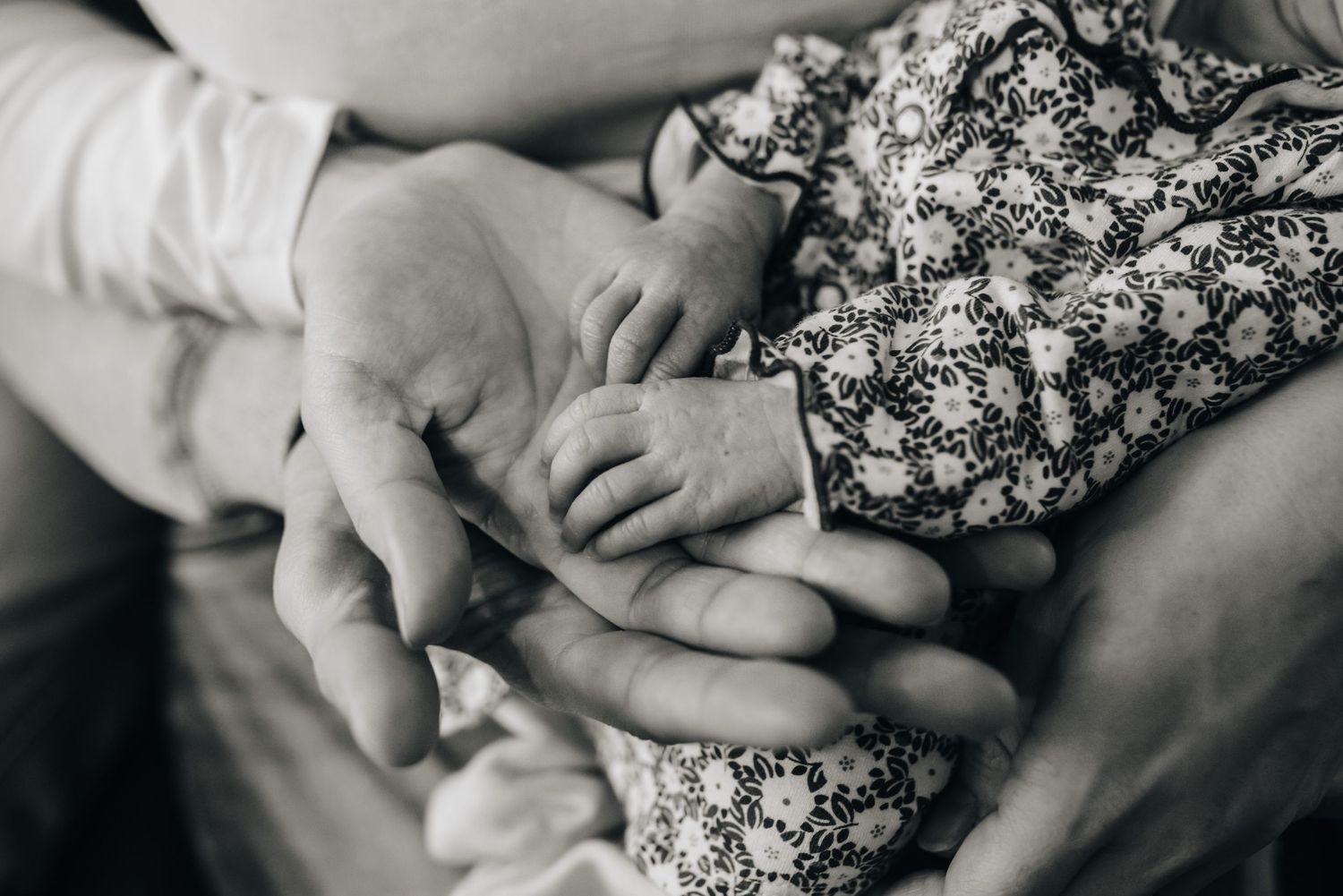 Black and white newborn photography with gentle hands and floral outfit.