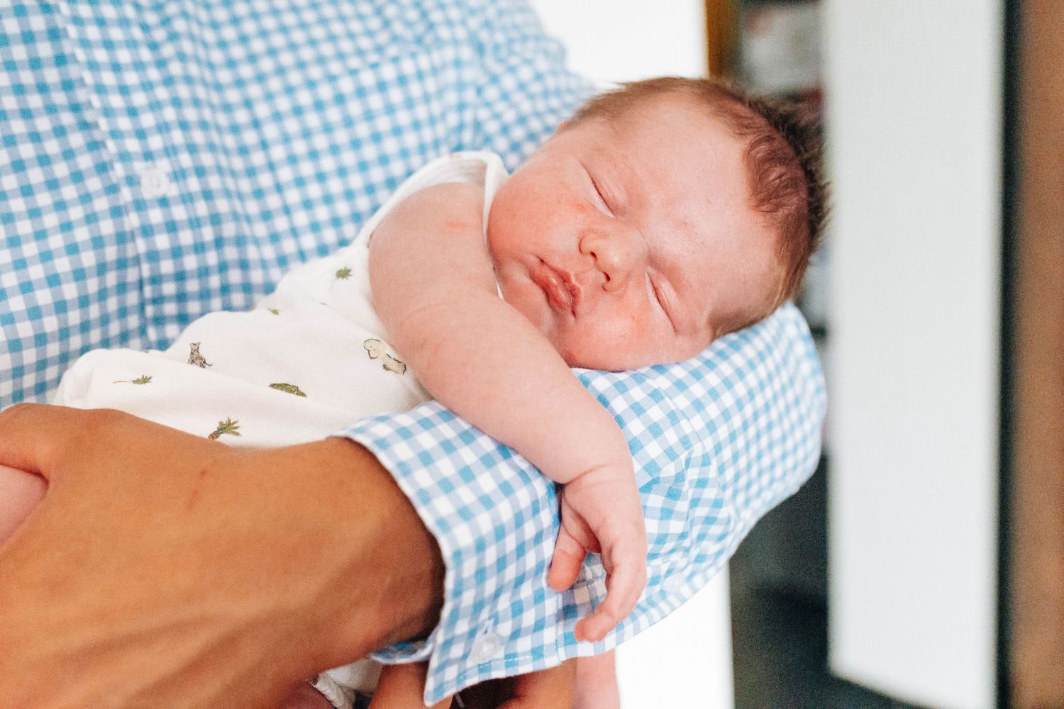 Sleeping baby in soft focus with blue gingham pattern visible.