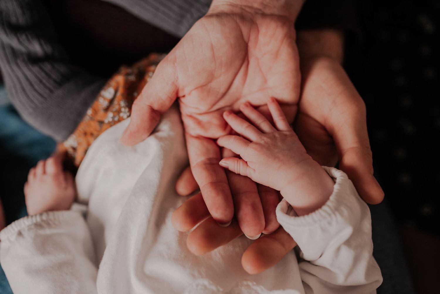 Close-up of gentle hands holding tiny newborn fingers.