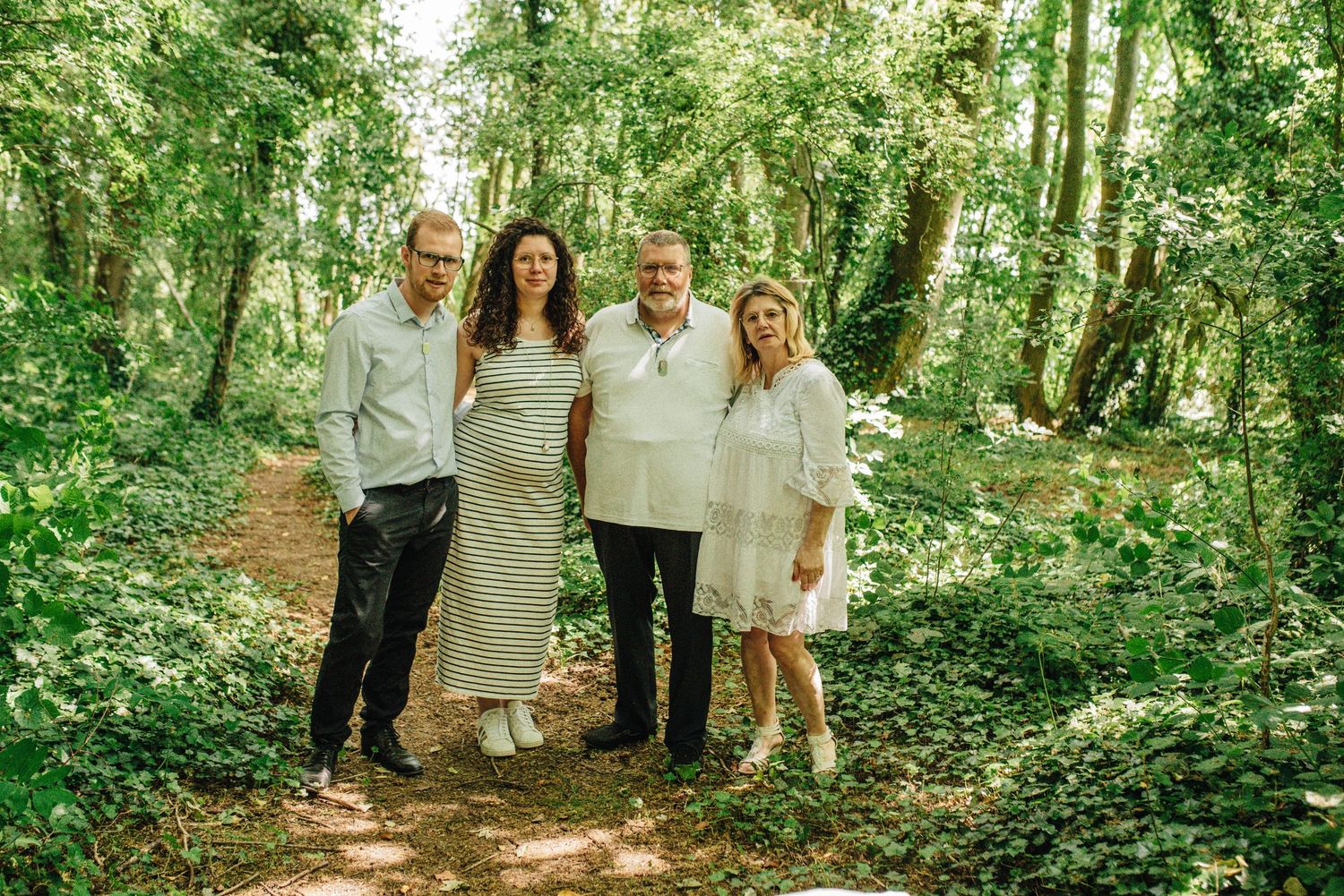 A group stands together on a forest path surrounded by lush green trees on a sunny day.