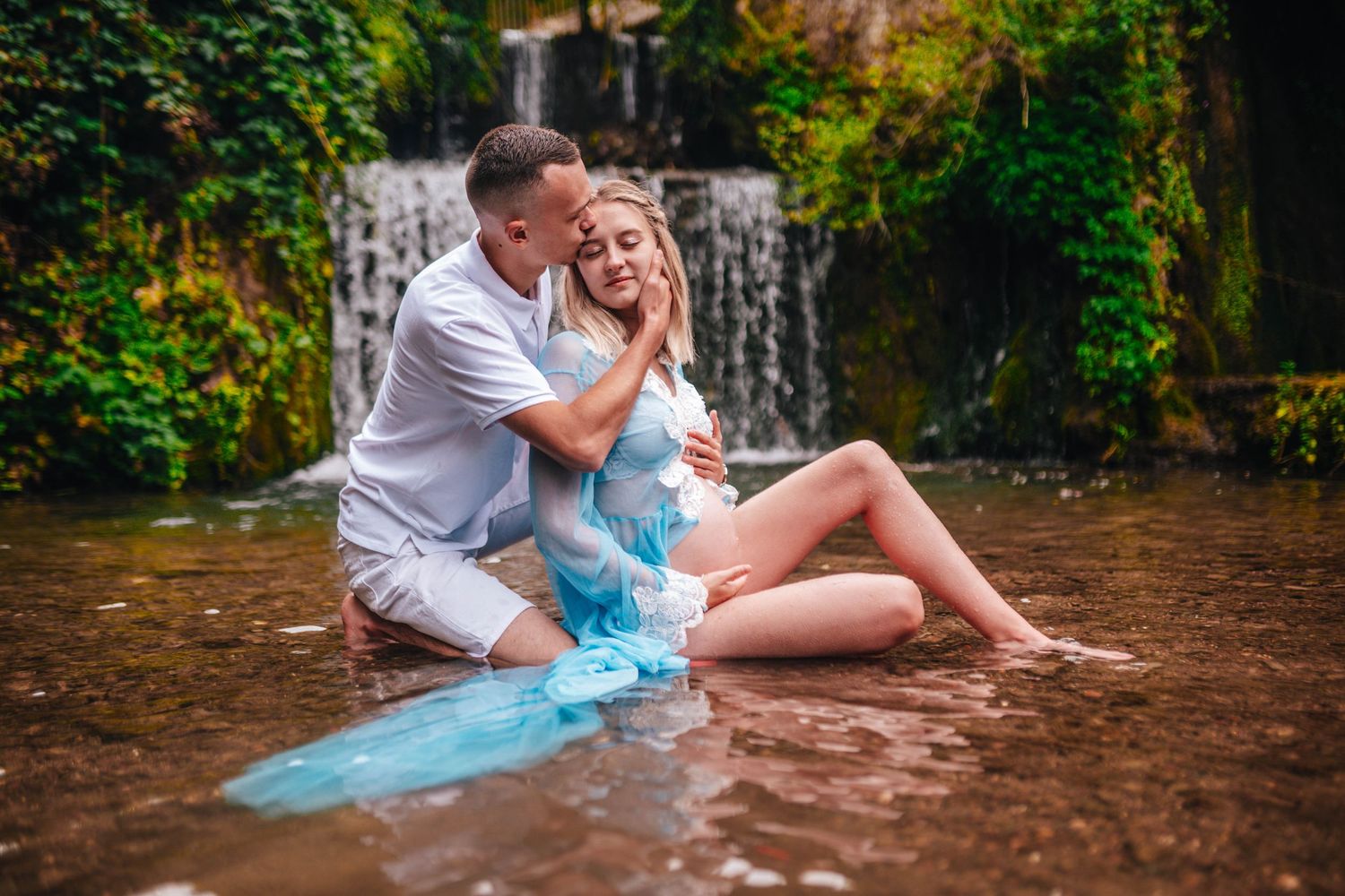 Couple sharing intimate moments near a waterfall in casual summer attire.