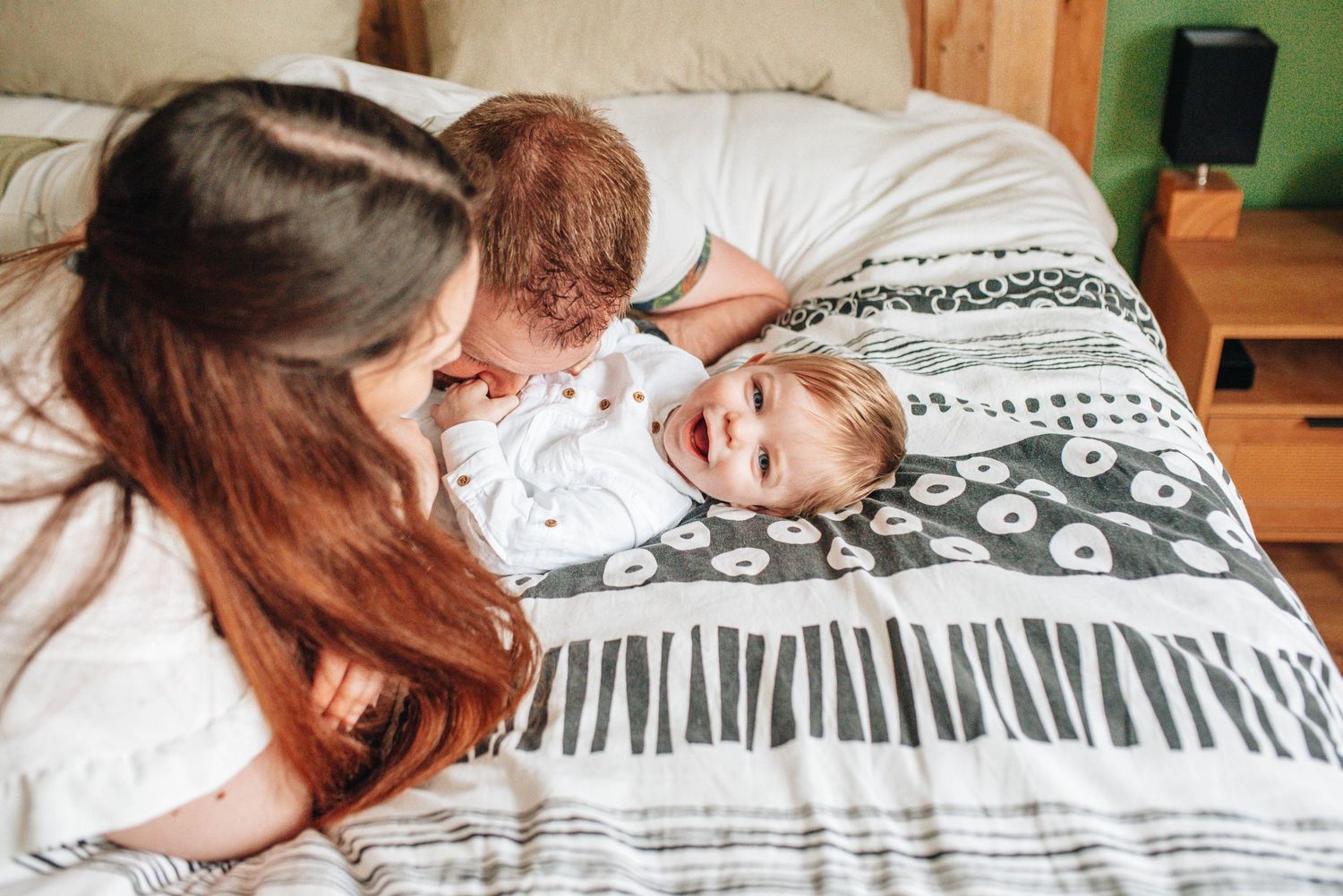 Family cuddles together on a cozy bed with striped bedding.
