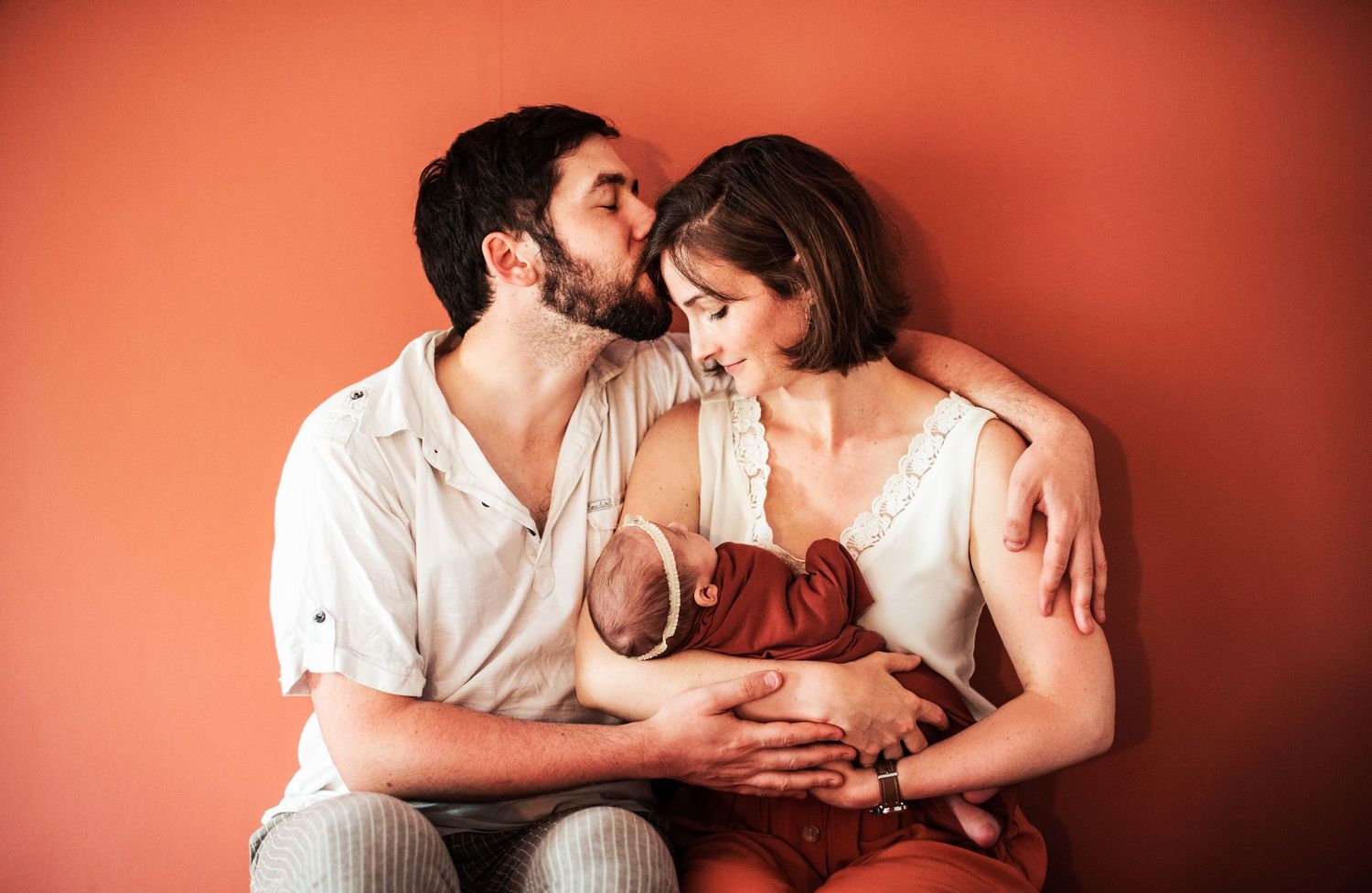 Tender family moments photographed in sequence against a coral red wall.