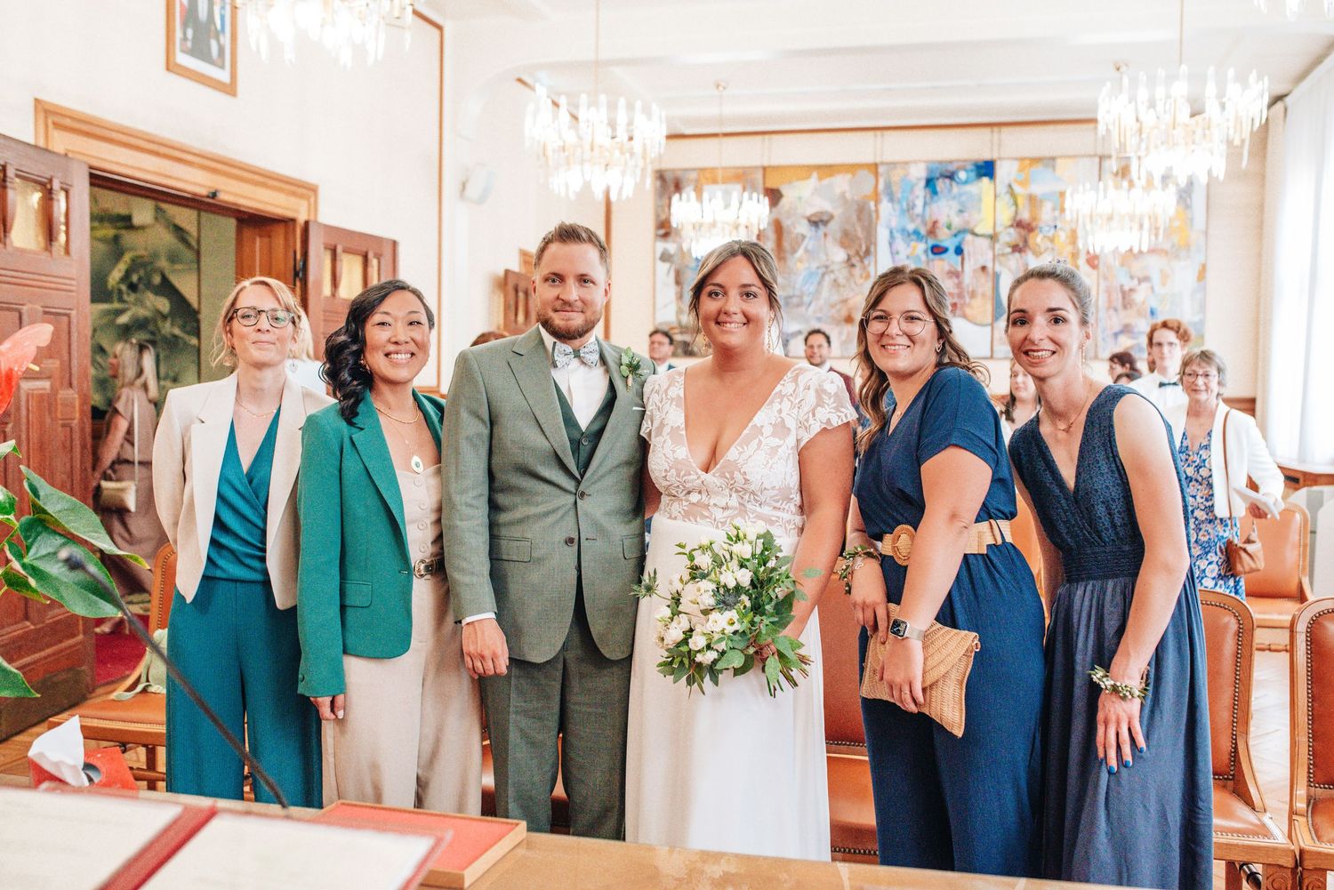 Wedding party poses in formal attire with green and blue color scheme in an elegant indoor setting.