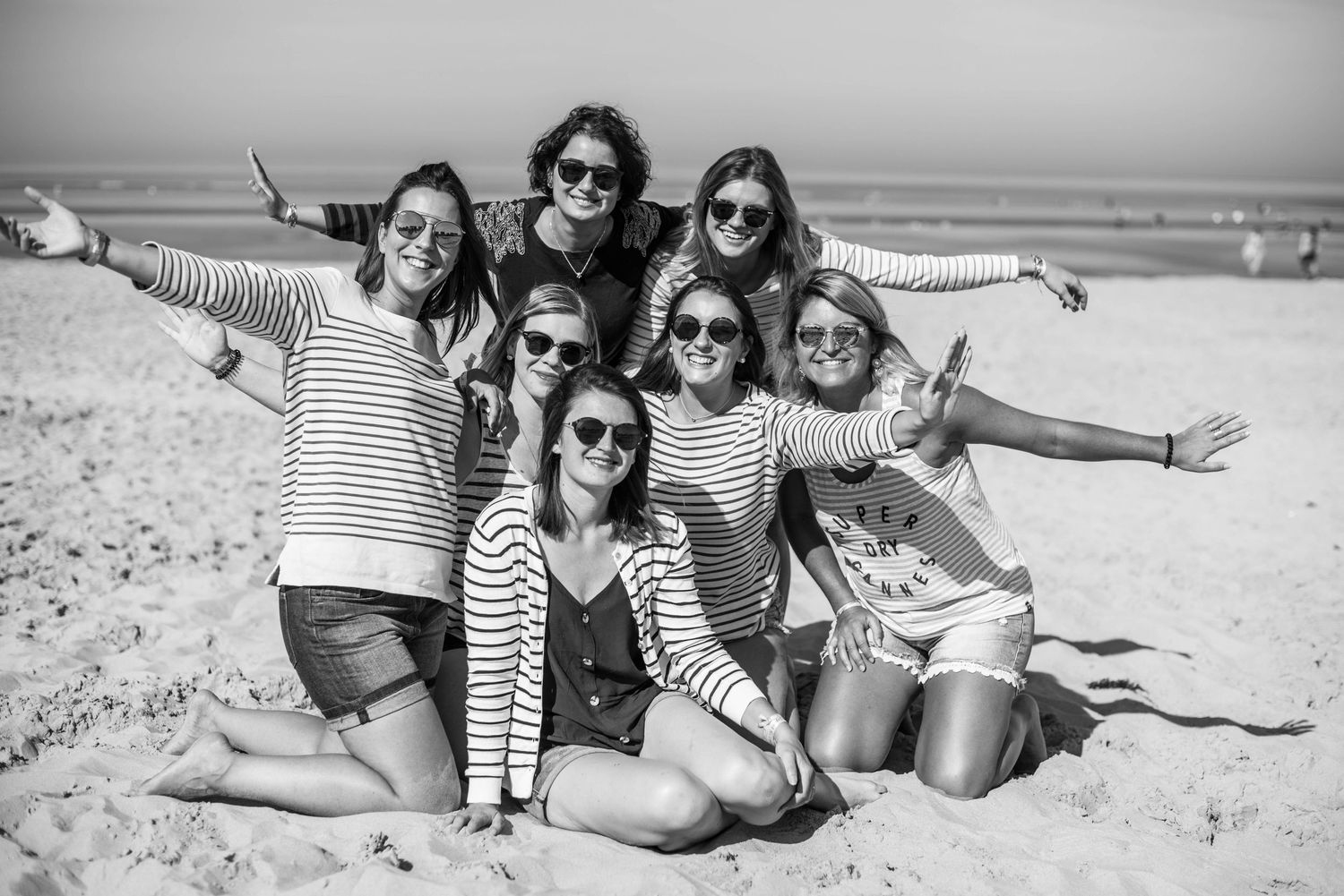 Group of friends pose playfully on beach in black and white photo.