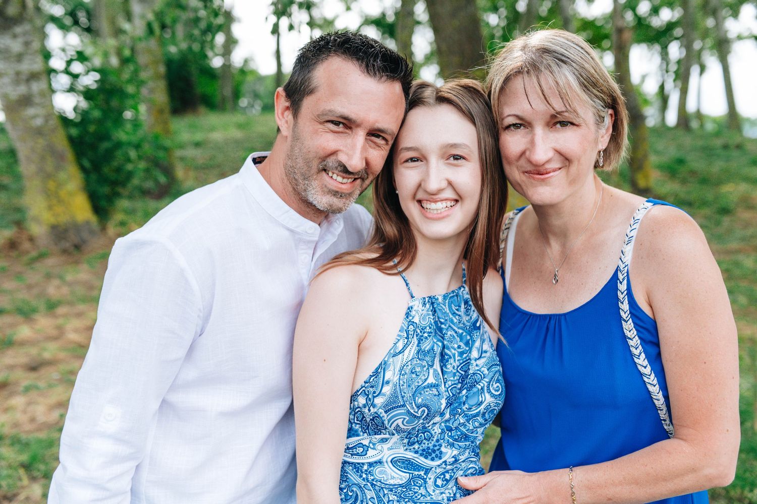 Family portrait session in coordinated blue and white outfits under green trees.