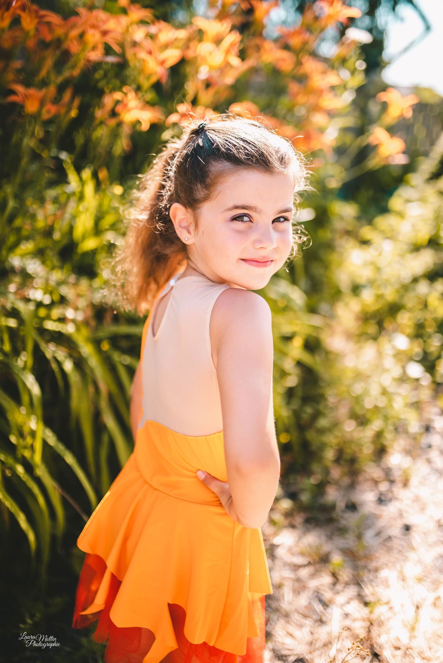 Summer portrait in orange ruffled dress with warm sunset lighting through trees.