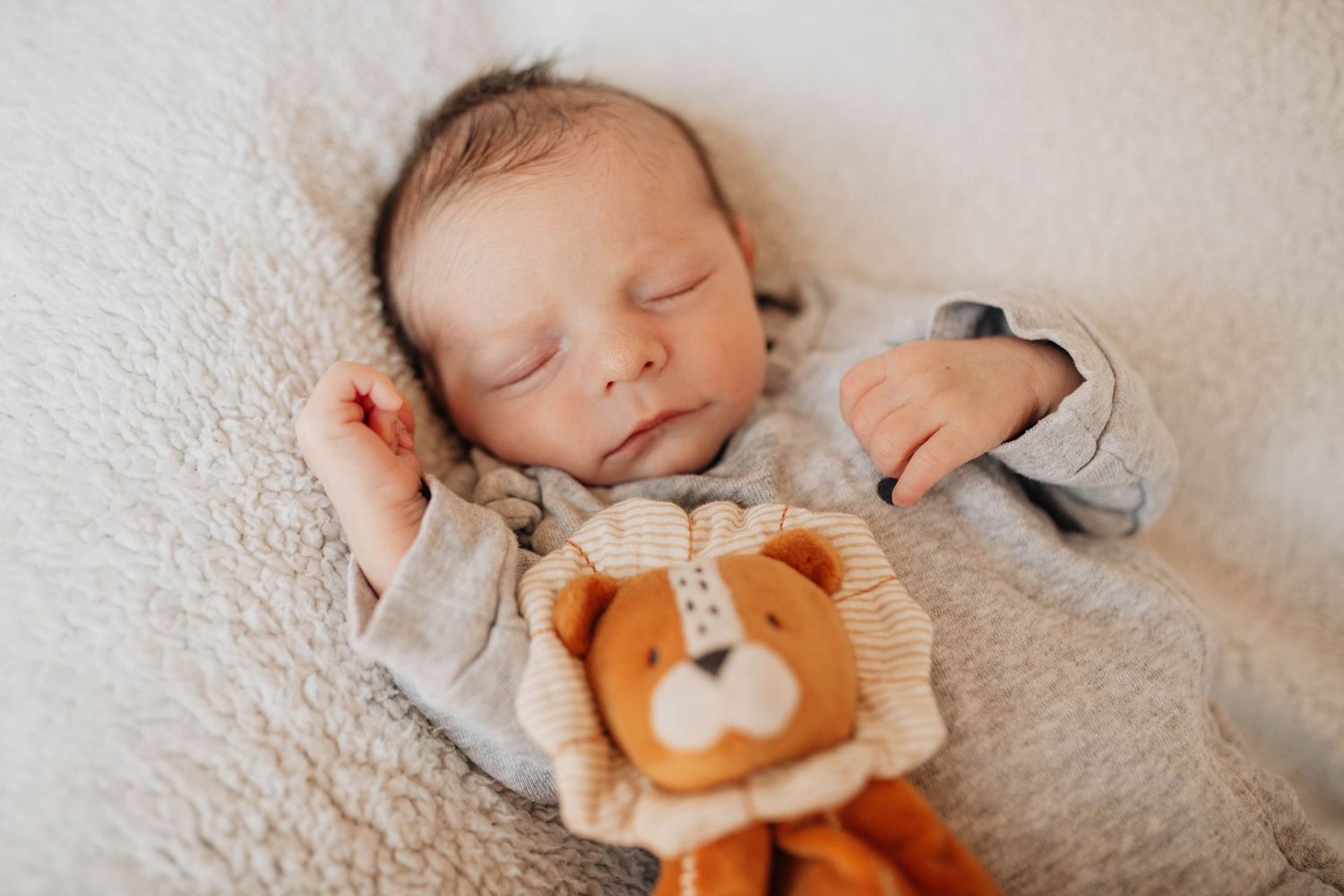 Sleeping newborn baby photographed with plush teddy bear on cream textured surface.