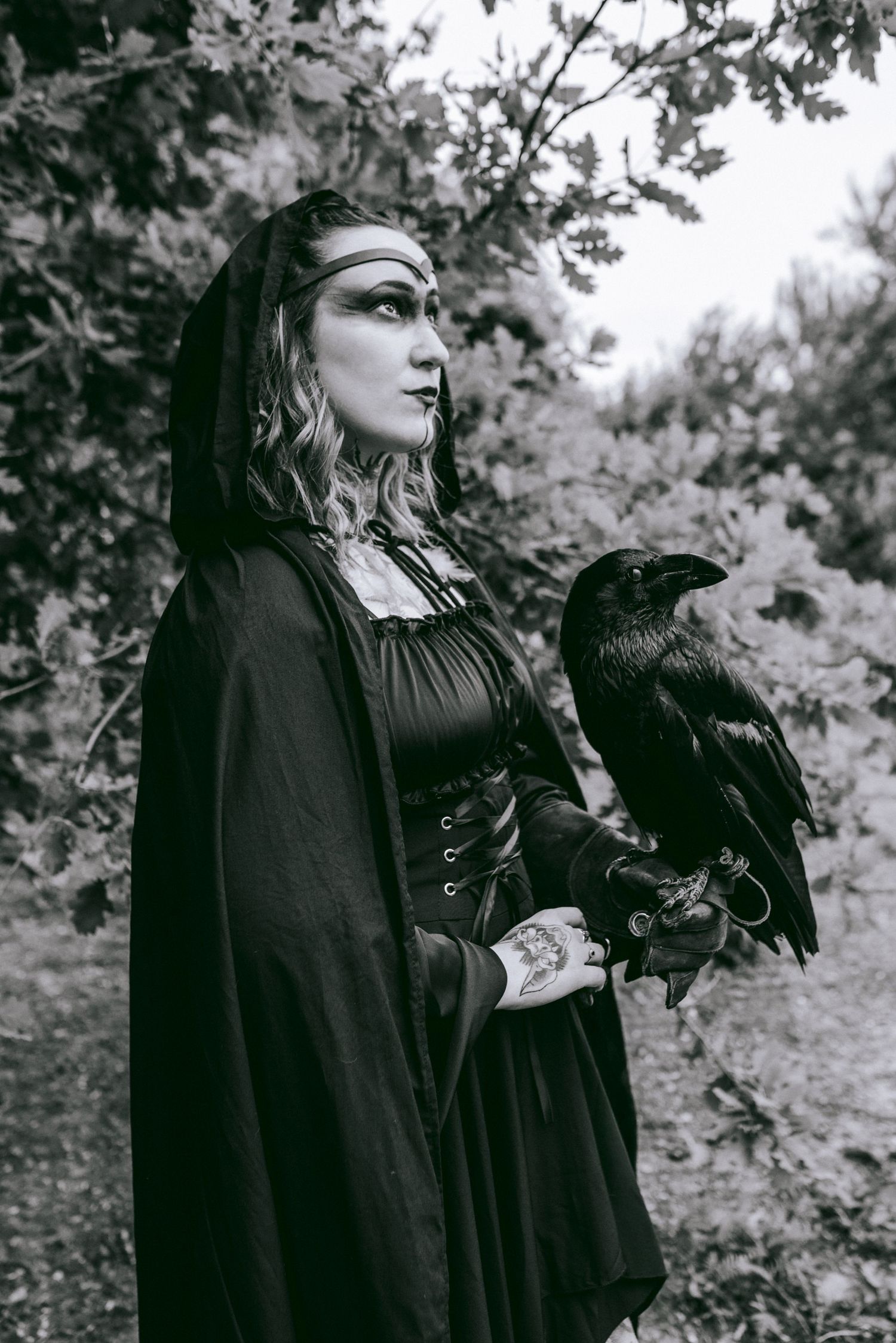 Figure in gothic black dress and dramatic makeup poses in moody forest setting.