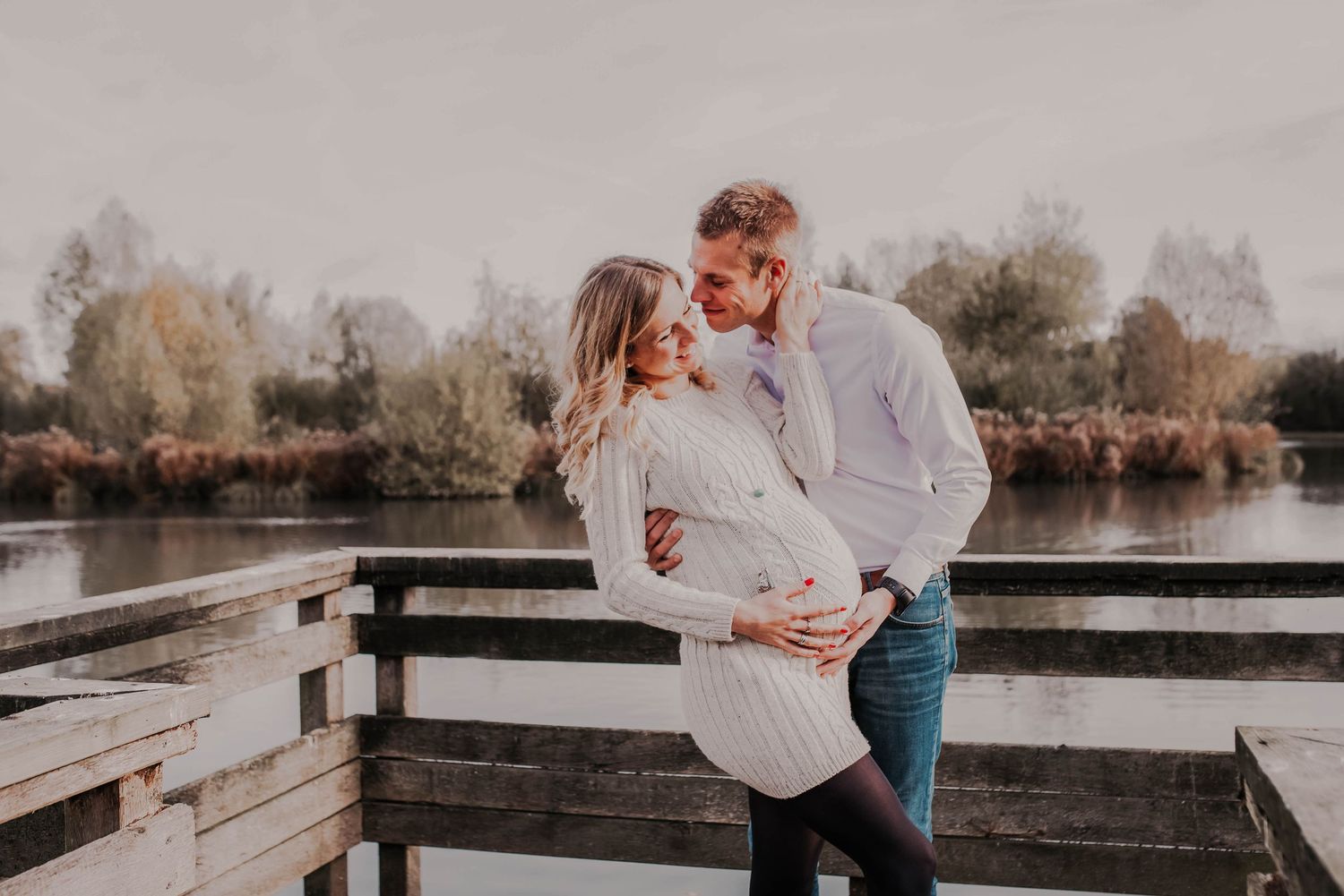 Romantic maternity photo of couple embracing on wooden dock at sunset.