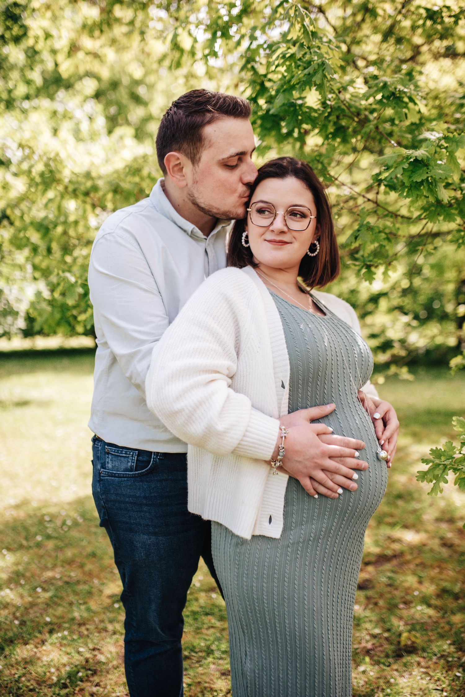 Couple sharing tender pregnancy announcement moments in sunlit garden setting.