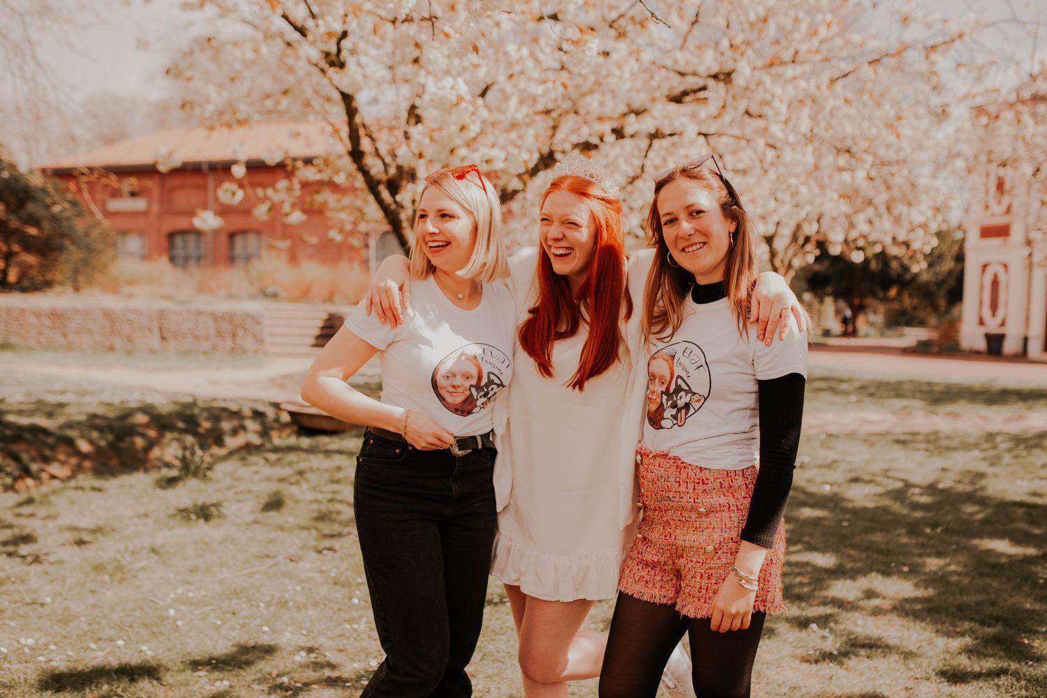 Three friends posing together outdoors under blooming spring trees.