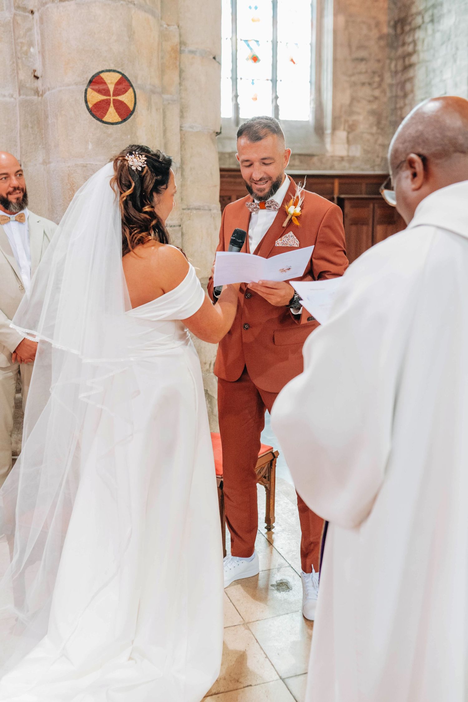 Wedding ceremony in a historic stone church with rustic decor and white-robed clergy.
