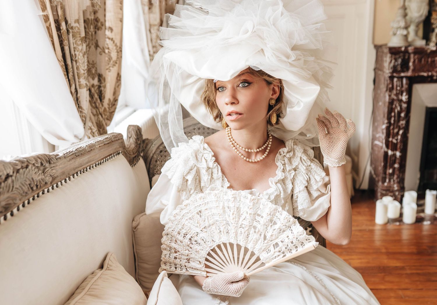 Vintage-inspired portrait in white dress with lace fan and ornate headpiece.