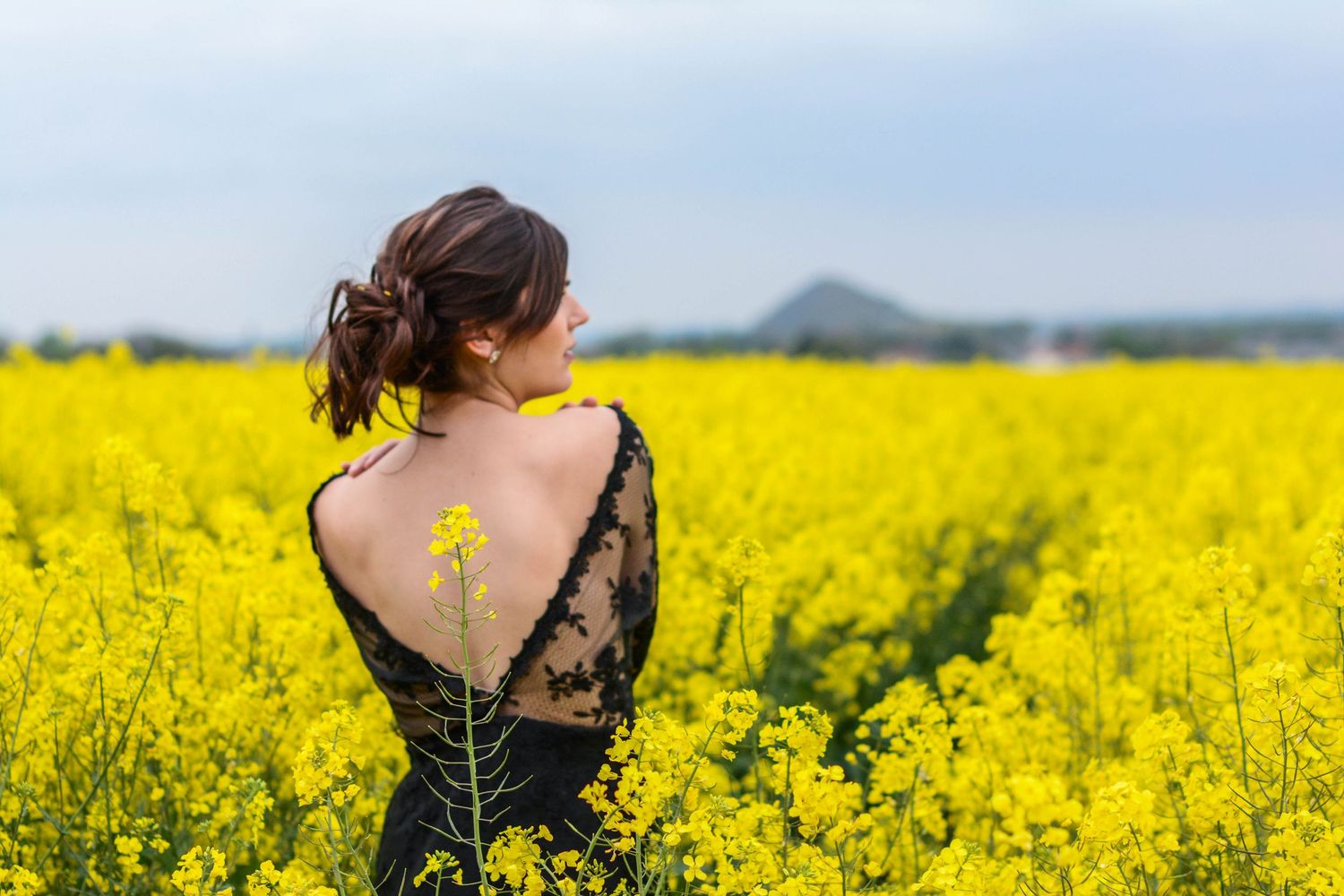 Person in dark dress poses against vibrant yellow canola flower field.