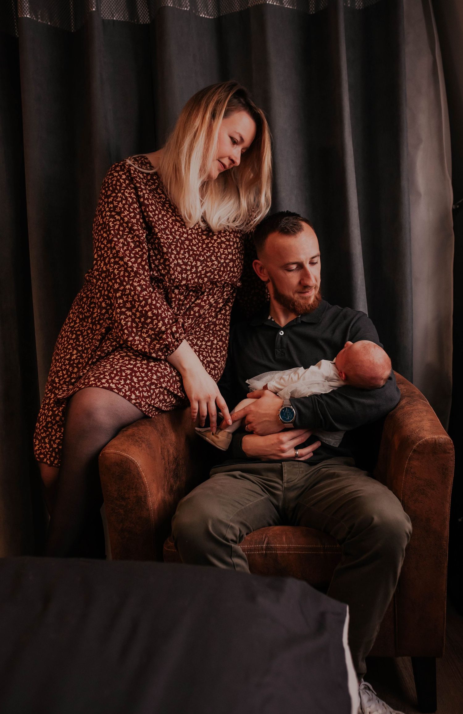 Intimate family moments captured on a brown armchair against dark curtains.