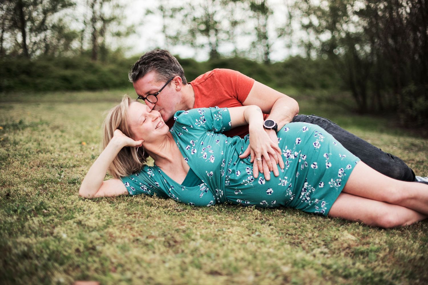 Couple lying in grass during outdoor maternity photoshoot.