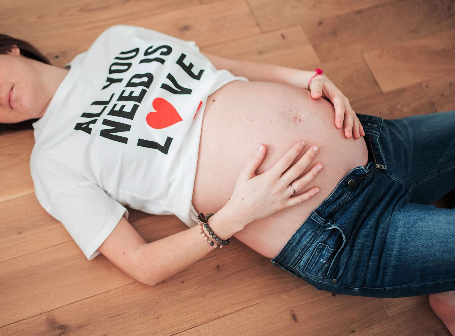 Expectant mother lying on wooden floor wearing All You Need is Love t-shirt.