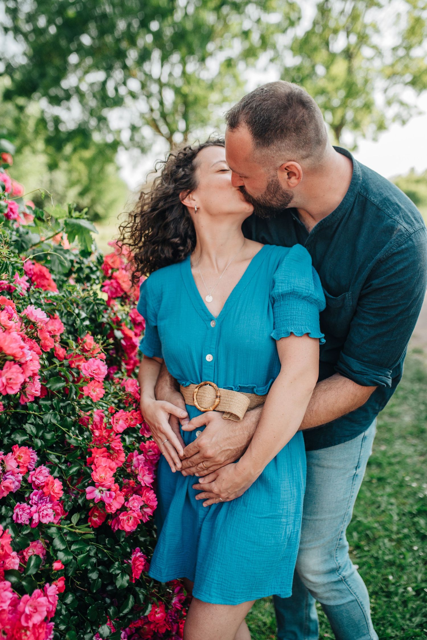 Romantic couple embraces near blooming pink roses in a garden setting.