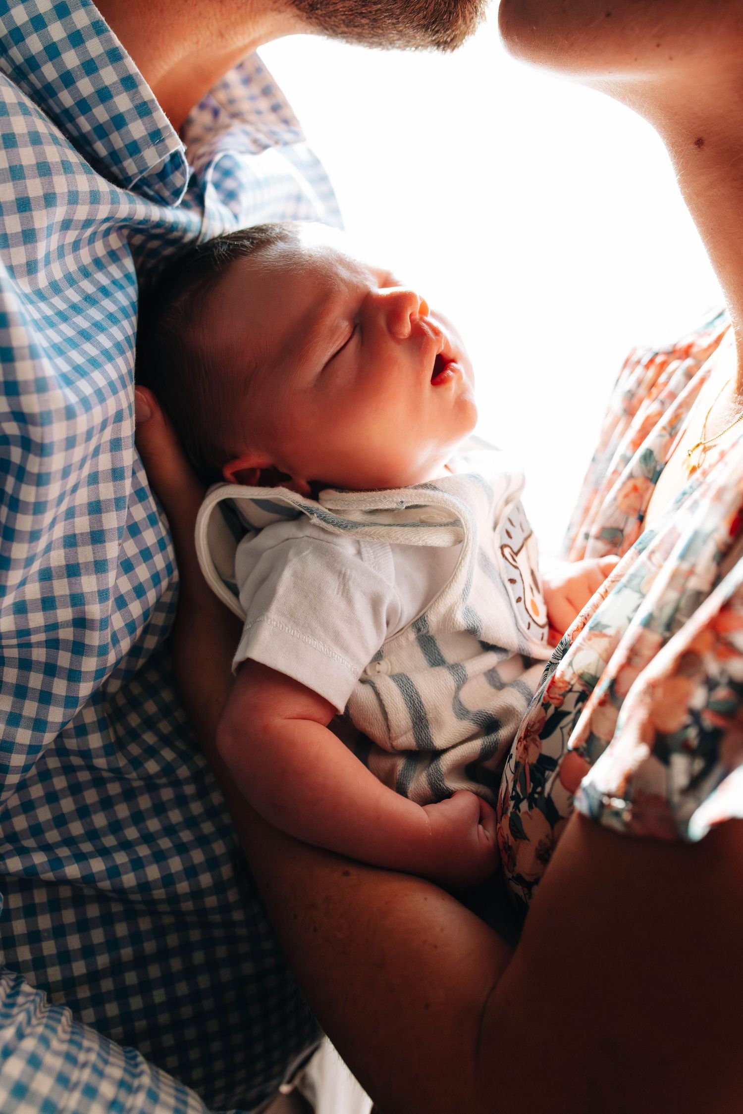 Baby sleeping peacefully against backlit blue gingham fabric.