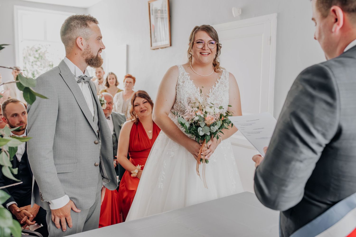 Wedding ceremony in bright indoor venue with guests watching couple exchange vows.