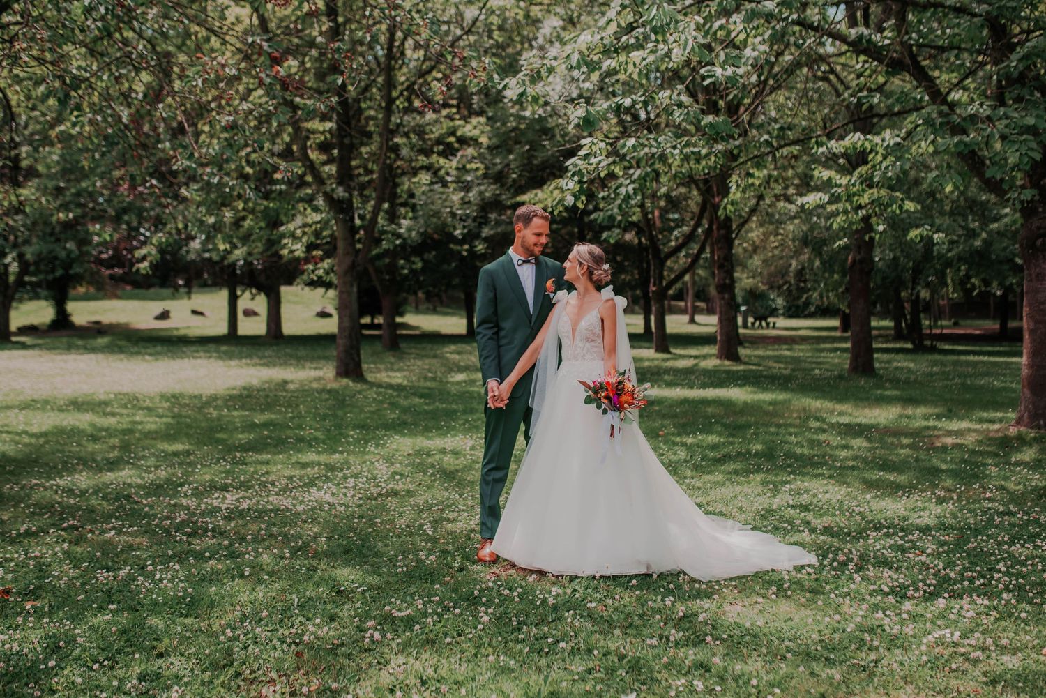 Newlyweds share intimate moments in a lush green park setting during their wedding photoshoot.