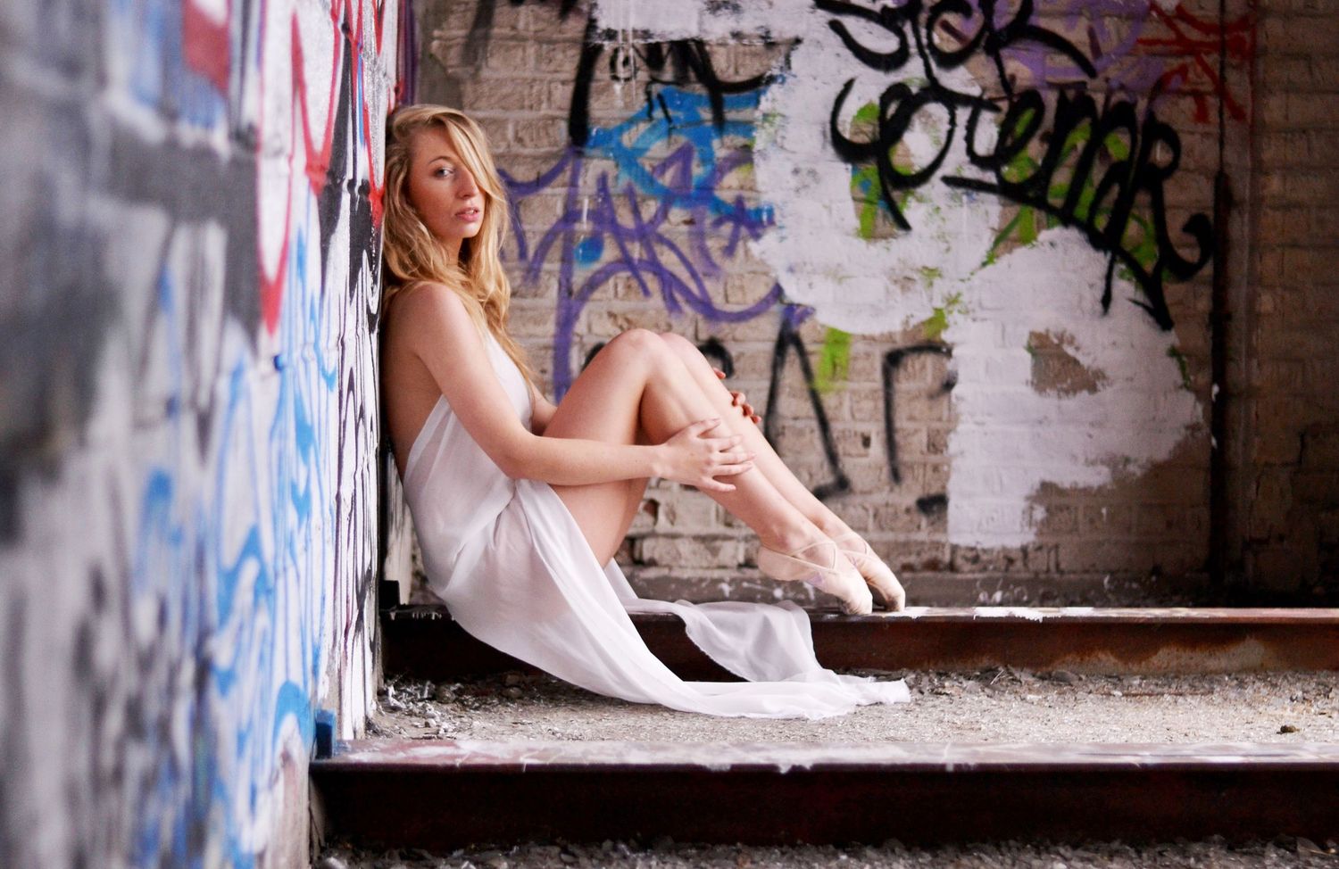 Person in white sitting against graffiti wall in urban setting.