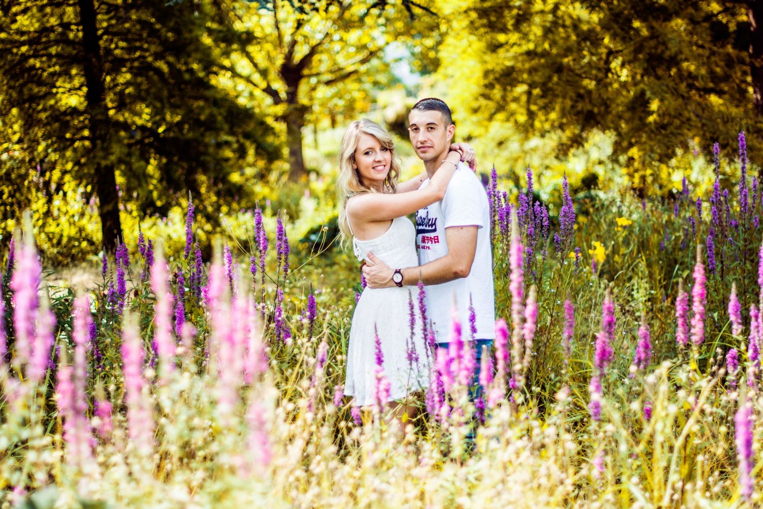Couple walking through meadow with purple wildflowers in golden sunlight.