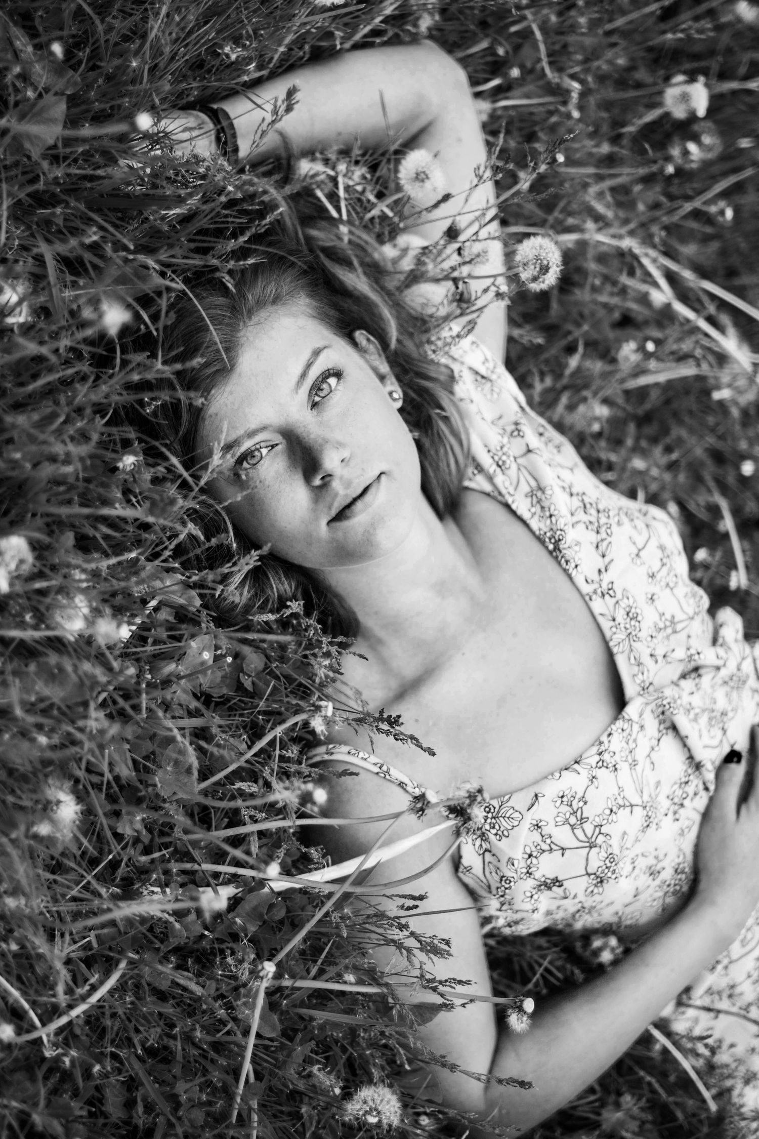 Artistic black and white portrait of someone lying in wildflowers wearing a floral dress.