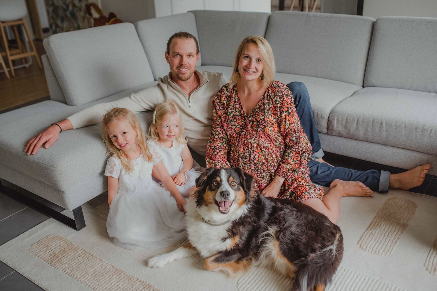 Family relaxing on white couch with their dog in bright modern living room.