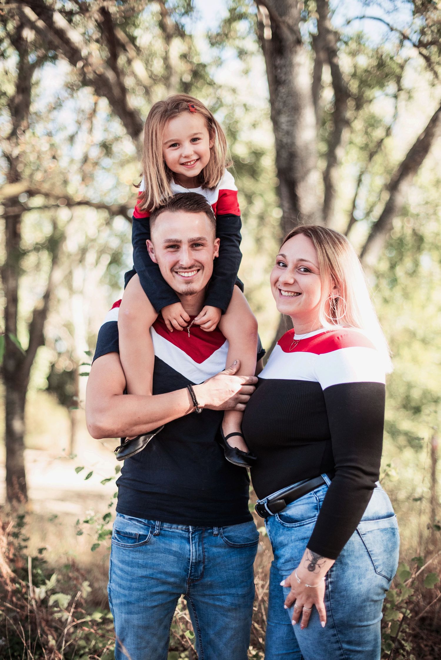 Family wearing coordinated outfits enjoying playful moments in wooded setting.